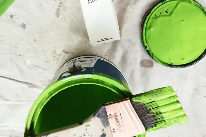 Un pinceau trempé dans de la peinture verte, à côté de deux pots de peinture verte et d'un tube de peinture blanche avec le mot 'hello' écrit dessus.