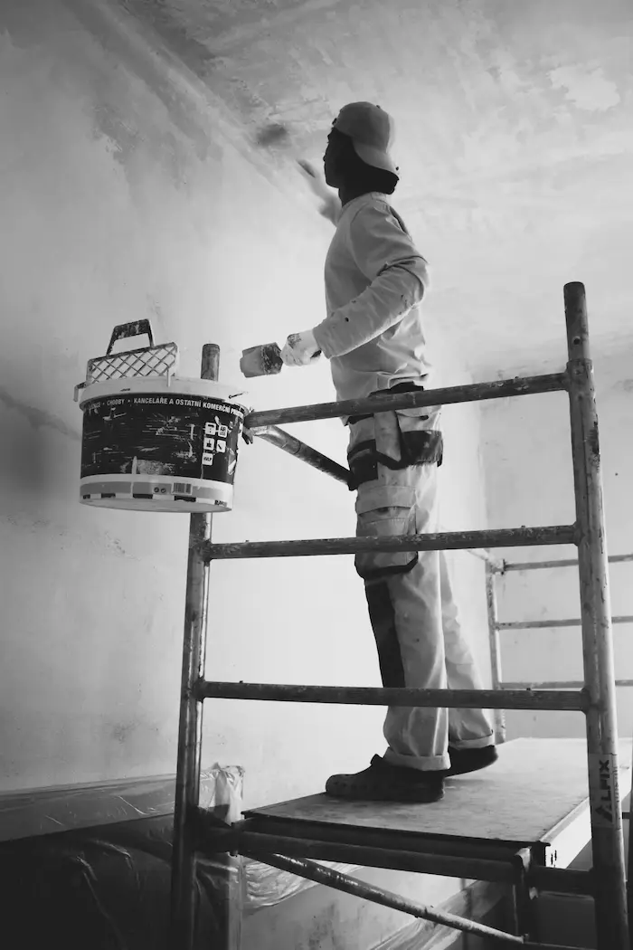 Un peintre en haut d'un échafaudage applique de la peinture au plafond.