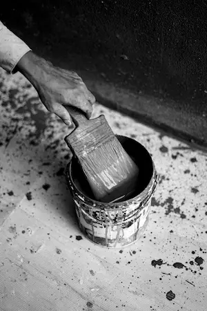 Une main tient un pinceau trempé dans un pot de peinture, avec des éclaboussures de peinture autour.