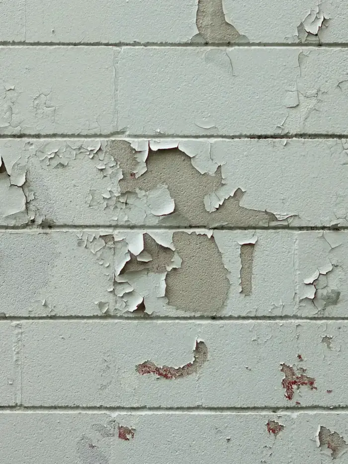 Un mur en briques avec de la peinture blanche écaillée, révélant des zones de briques nues et des taches de rouille.