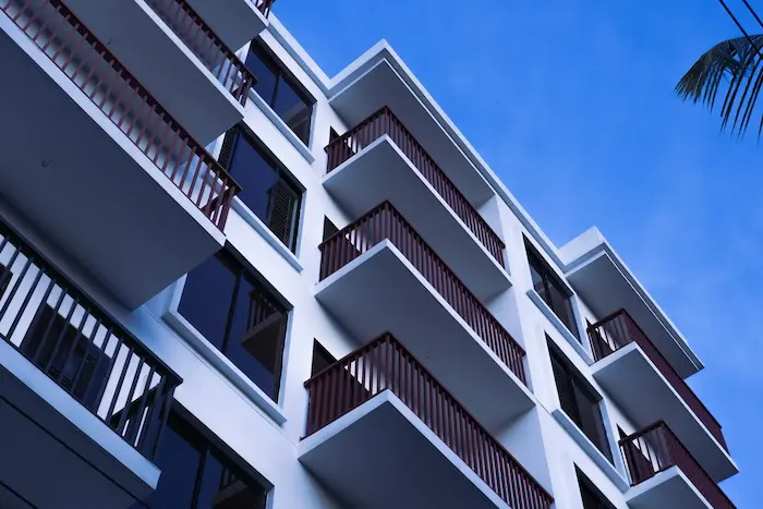 Façade d'un immeuble moderne avec plusieurs balcons en bois et des fenêtres, sous un ciel bleu clair.