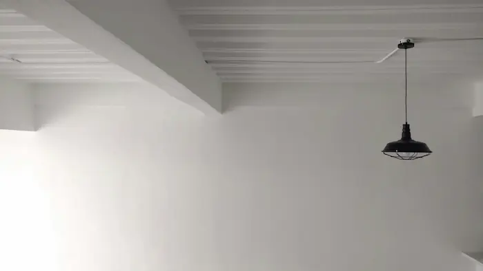 Un mur blanc avec un plafond à moulures et une suspension noire pendue au plafond.