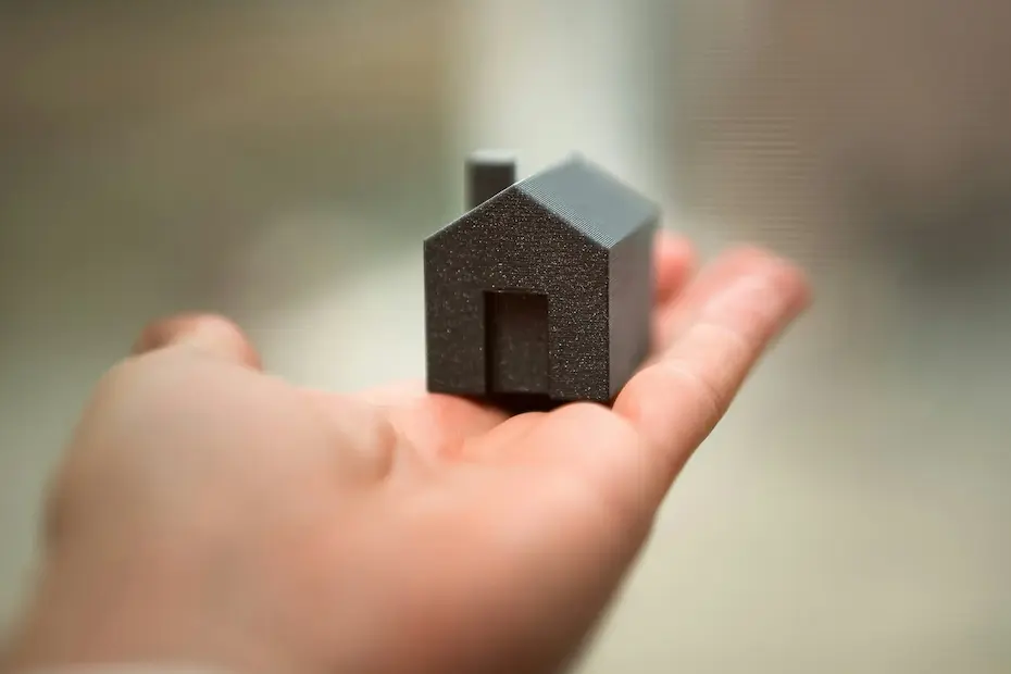 Une main tenant une petite maison en bois noir avec une porte et une cheminée.